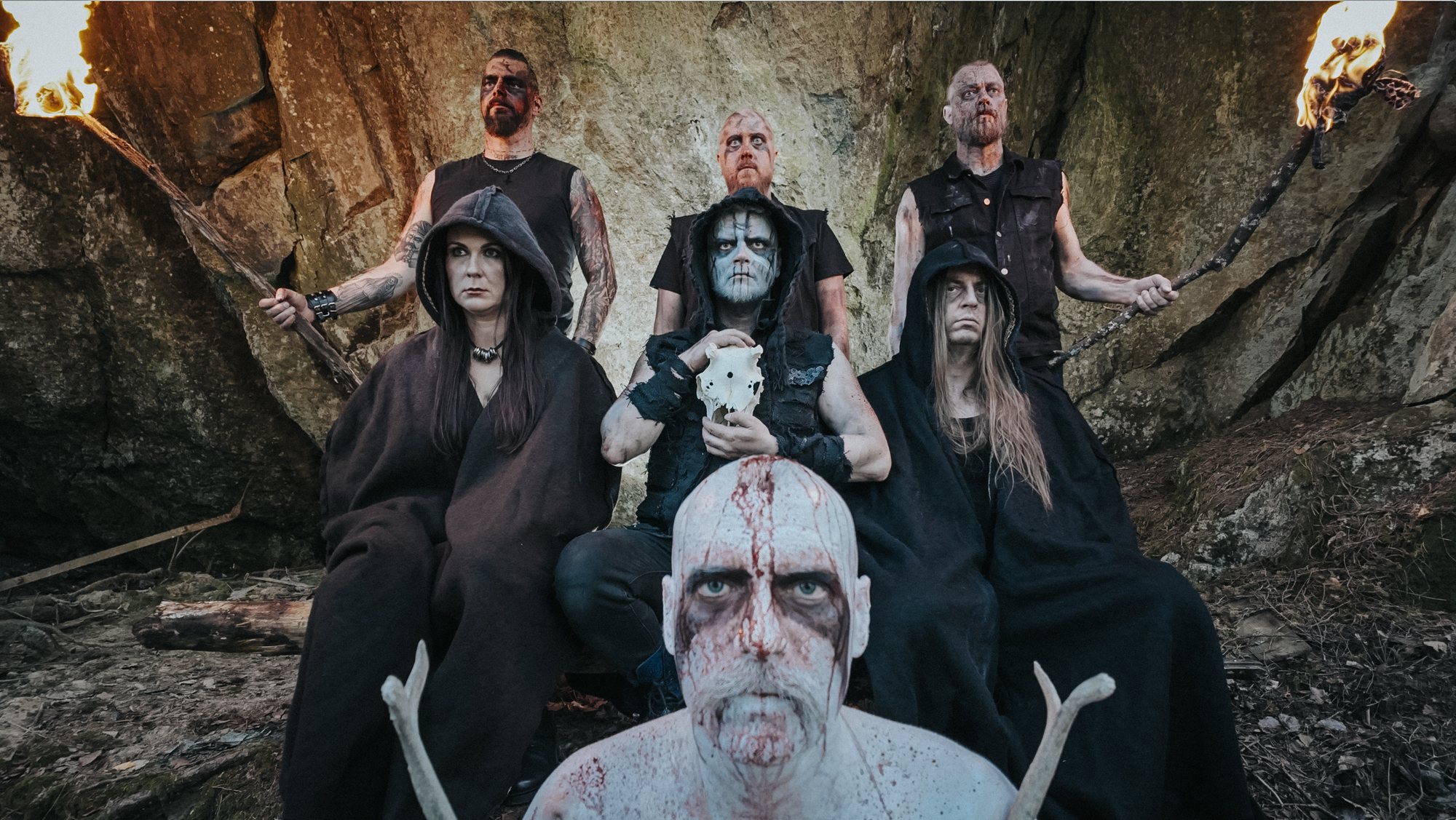 The Mist From The Mountains: seven band members in corpse paint and hooded cloaks among rocks, with torches